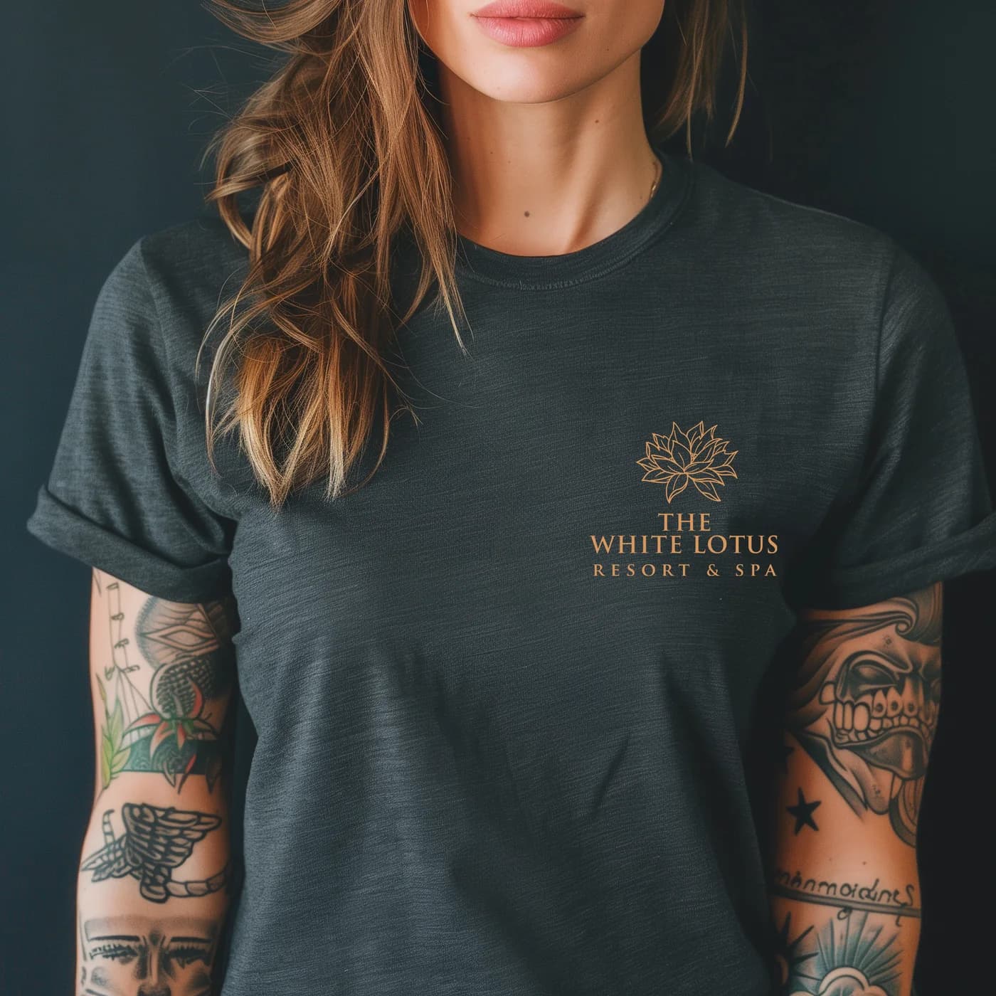Close-up of a heather charcoal tee with a copper lotus and The White Lotus Resort & Spa logo on the left chest.