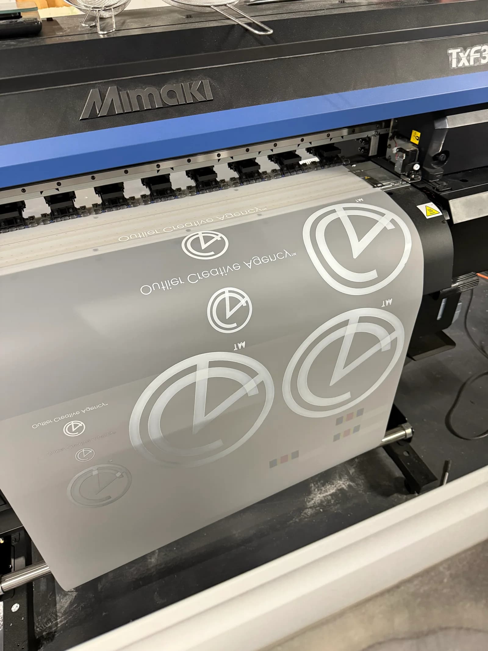 Outlier Creative Agency logos arranged on transfer film in a Mimaki printer.